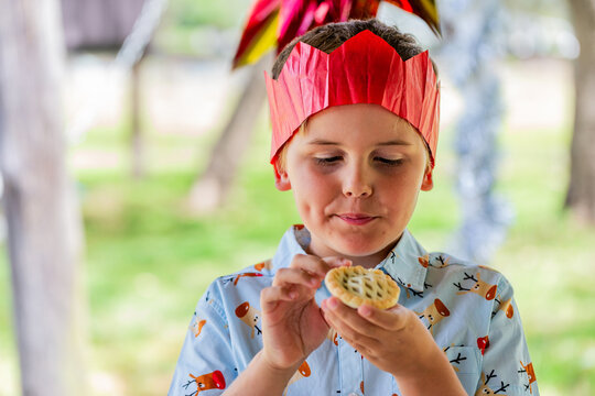 Aussie child staring hungrily at fruit mince pie in hands while wearing paper crown at Christmas