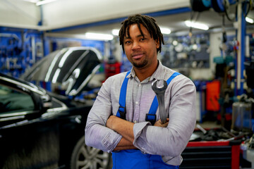 An African-American mechanic confidently posing with tools in hand in his workshop.