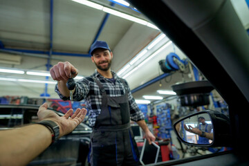 Sealing the deal with a smile: A white mechanic passes car keys to a happy customer, embodying quality service and customer satisfaction in the workshop. - obrazy, fototapety, plakaty