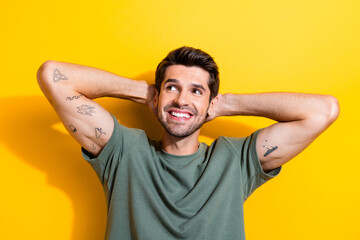 Fototapeta na wymiar Photo of dreamy cool man with bristle dressed khaki t-shirt arms behind head look at offer empty space isolated on yellow color background
