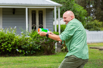 Happy dad in water fight game with family in yard of weatherboard home