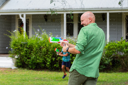 Happy dad in water fight game with sons in yard of weatherboard home
