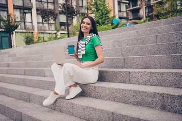 Fototapeta premium Photo of shiny sweet lady wear green t-shirt sitting stairs enjoying coffee communicating modern device outside urban city street