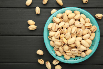 Plate with pistachios on black wooden background.