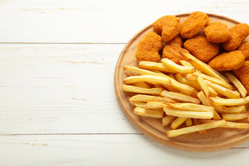 Plate of chicken nuggets with french fries on cutting board on white background.