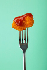 Chicken nugget with ketchup on a fork on mint background. Vertical photo