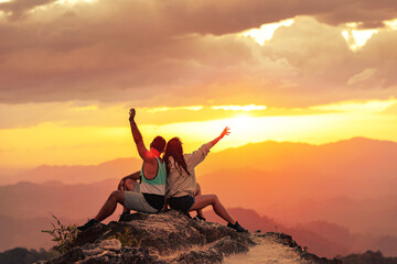 Happy couple enjoys sunset and sits with open arms at mountain top
