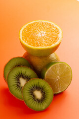 Composition of Sliced orange, lemon and kiwi fruits in a clean orange background in front view