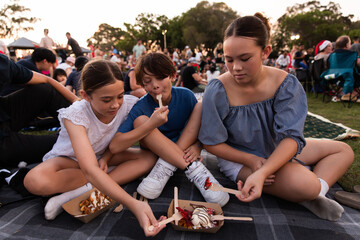 siblings sharing food on a picnic rug in the park