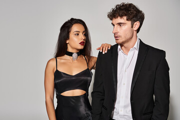 gorgeous woman with brunette hair and red lips posing near man in black attire on grey background