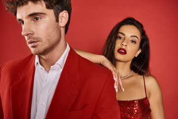 focus on attractive and young woman with bright lipstick near blurred man on red background