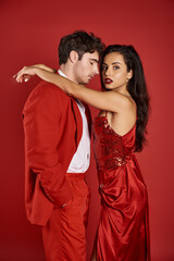 sophisticated and brunette young woman in sexy dress embracing handsome man on red background