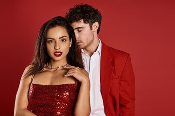 handsome man in formal wear seducing beautiful young woman in shiny dress on red background