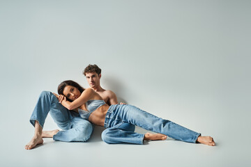 Fototapeta na wymiar brunette young woman in satin bra leaning on sexy shirtless man in blue jeans on grey background