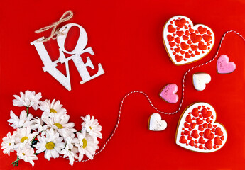 Happy Valentine's Day greeting card. Two gingerbreads in the form of hearts and white chrysanthemum flowers on a red background.