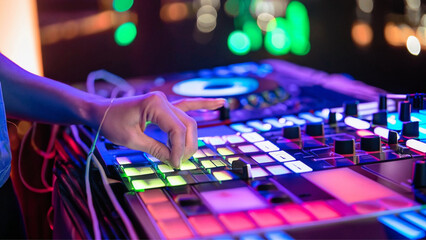 Detalhe da mão de um dj manuseando os botões de um controlador, em uma festa com muitas luzes...