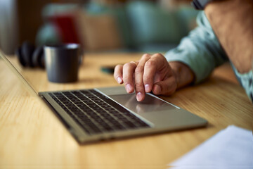 Close-up of male hand using a touchpad of a laptop for work on a wooden desk.