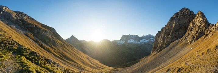 Sunrise over a tranquil mountain valley with light piercing through peaks