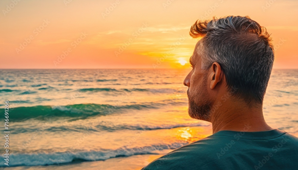 Sticker  a man standing on top of a beach next to the ocean under a cloudy sky with the sun setting over the ocean and a wave coming in front of him.