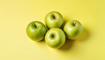  a group of four green apples sitting on top of each other on top of a yellow surface with one green apple in the middle of the middle of the group.