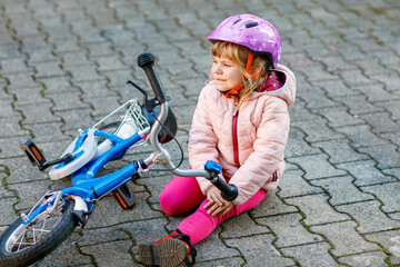Cute little girl sitting on the ground after falling off her bike. Upset crying preschool child...
