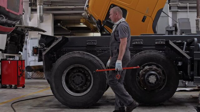 Professional locksmith auto mechanic moves through the workshop with a tool against the background of large cargo trucks