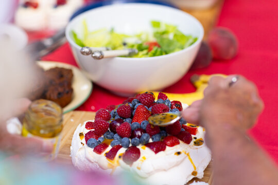 first person view of spooning passionfruit pulp over a pavlova topped with fresh berries