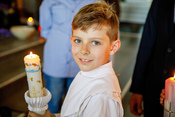 Little kid boy receiving his first holy communion. Happy child holding Christening candle....