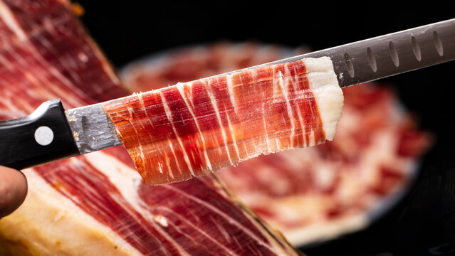 Preparing a plate of Spanish cured acorn fed Iberian ham cut with a knife for tasting at an event. Real image, Jam&oacute;n ib&eacute;rico serrano