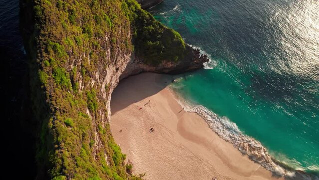 Famous Kelingking T-Rex sightseeing beach landmark at Nusa Penida Island, Bali, Indonesia. Aerial drone footage at sunset with beautiful waves