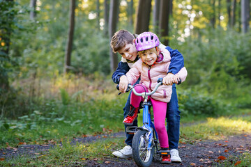 Cute little preschool girl in safety helmet riding bicycle. School kid boy, brother teaching happy...