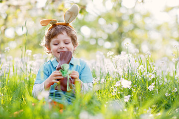 Cute little kid boy with Easter bunny ears celebrating traditional feast. Happy child eating...