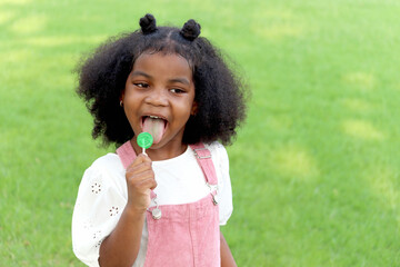Portrait of happy smiling African girl with black curly hair sticking out tongue while eating sweet...