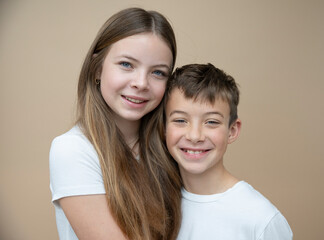 beautiful pretty 14 years old girl with her cute and cool 11 years old brother in front of brown background, brother and sister love