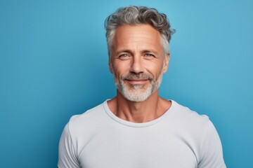 Obraz premium Portrait of a tender man in his 50s dressed in a casual t-shirt against a pastel blue background. AI Generation
