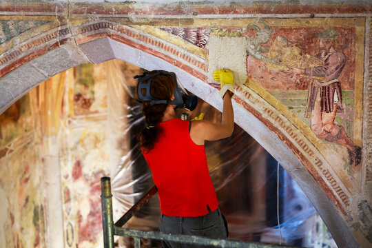 Restoration Process of Special Chemical Applications on a Church Arch Wall Ancient Fresco By Professional Female Restorer Wearing a Protective Gas Mask While Working