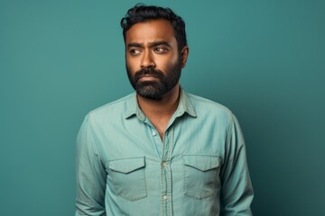 Portrait of a content indian man in his 30s sporting a versatile denim shirt against a pastel teal background. AI Generation