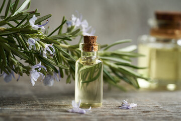 A transparent bottle of aromatherapy essential oil with fresh blooming rosemary plant