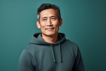 Obraz premium Portrait of a tender asian man in his 40s wearing a thermal fleece pullover against a pastel teal background. AI Generation
