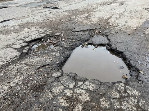 Pit with puddle on the asphalt road cover. Close-up shot.