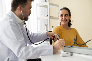 Caucasian Doctor using sphygmomanometer with stethoscope checking blood pressure to Latin woman...