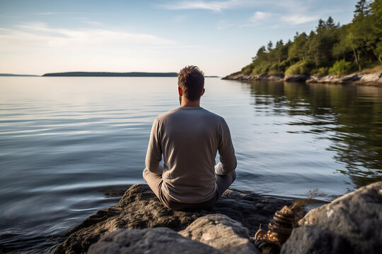 Young man sitting on a rock by the lake and looking at the horizon