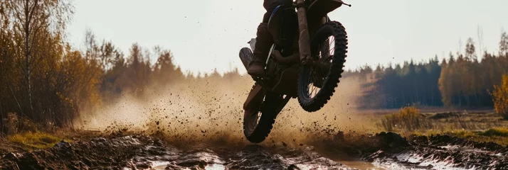 Deurstickers Motocross rider jumping over a muddy puddle in the forest. Motocross. Enduro. Extreme sport concept. © John Martin