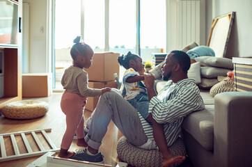 Father playing with two young daughters in new home with moving boxes
