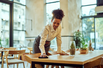 An African waitress, cleaning tables at the restaurant, working alone.