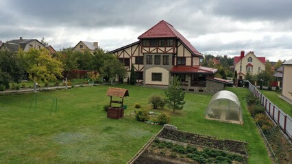 Naklejka premium Large house, cottage with red tiled roof in English style with a plot against a gloomy sky. Green grass in front of the house in Europe. Soccer goal on a private plot.
