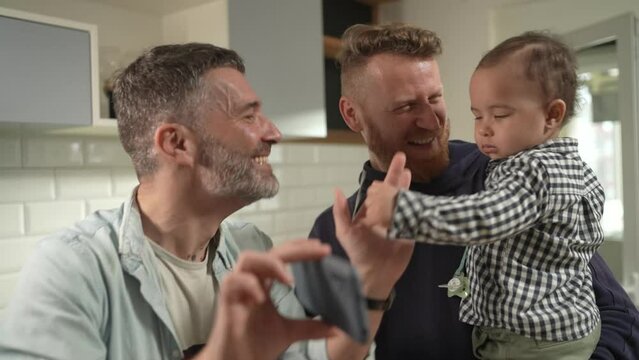 Gay male couple with child dancing in home kitchen