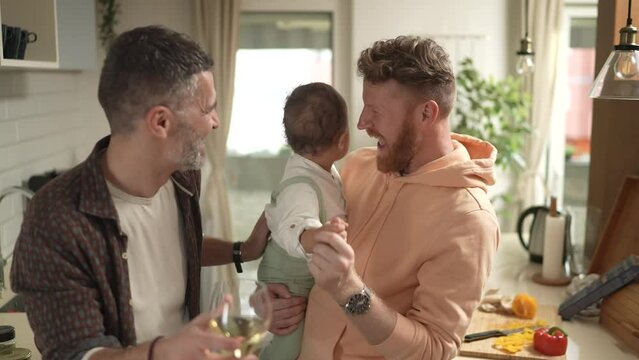 Gay male couple with child dancing in home kitchen