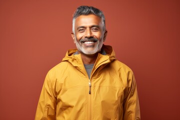 Obraz premium Portrait of a satisfied indian man in his 50s wearing a lightweight packable anorak against a soft brown background. AI Generation