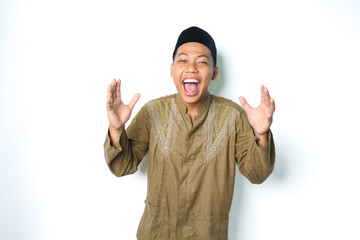 excited asian muslim man wearing islamic dress screaming with raised hand and looking at camera...